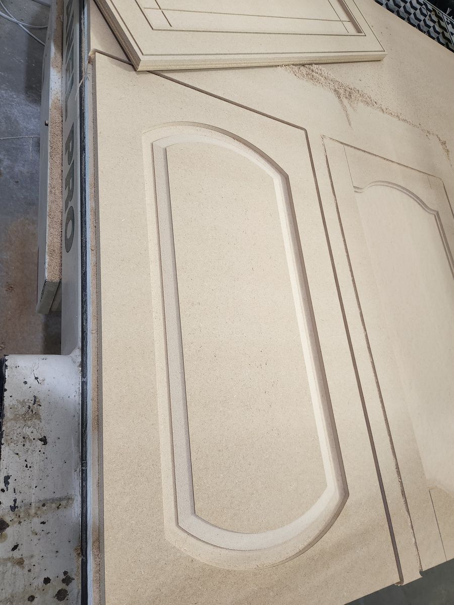 Arched-top and cathedral-top MDF cabinet doors still in the sheet on the CNC table after cutting