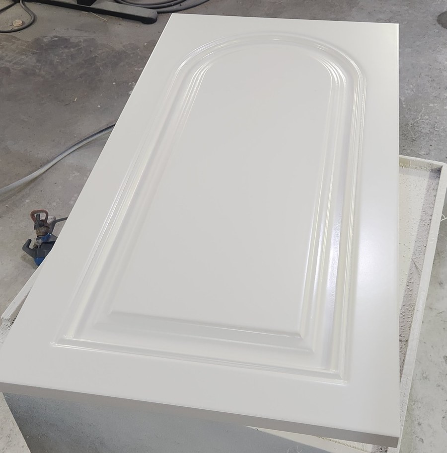 Painted one-piece MDF cabinet door with an arched raised panel, fresh off the spray booth in a cabinet shop